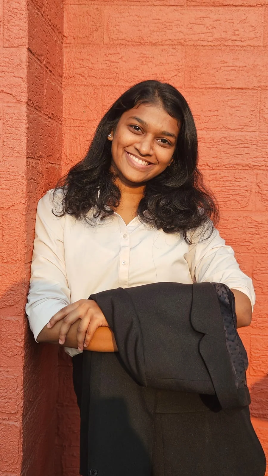 Lakshmi B Uday smiling in front of an orange brick wall